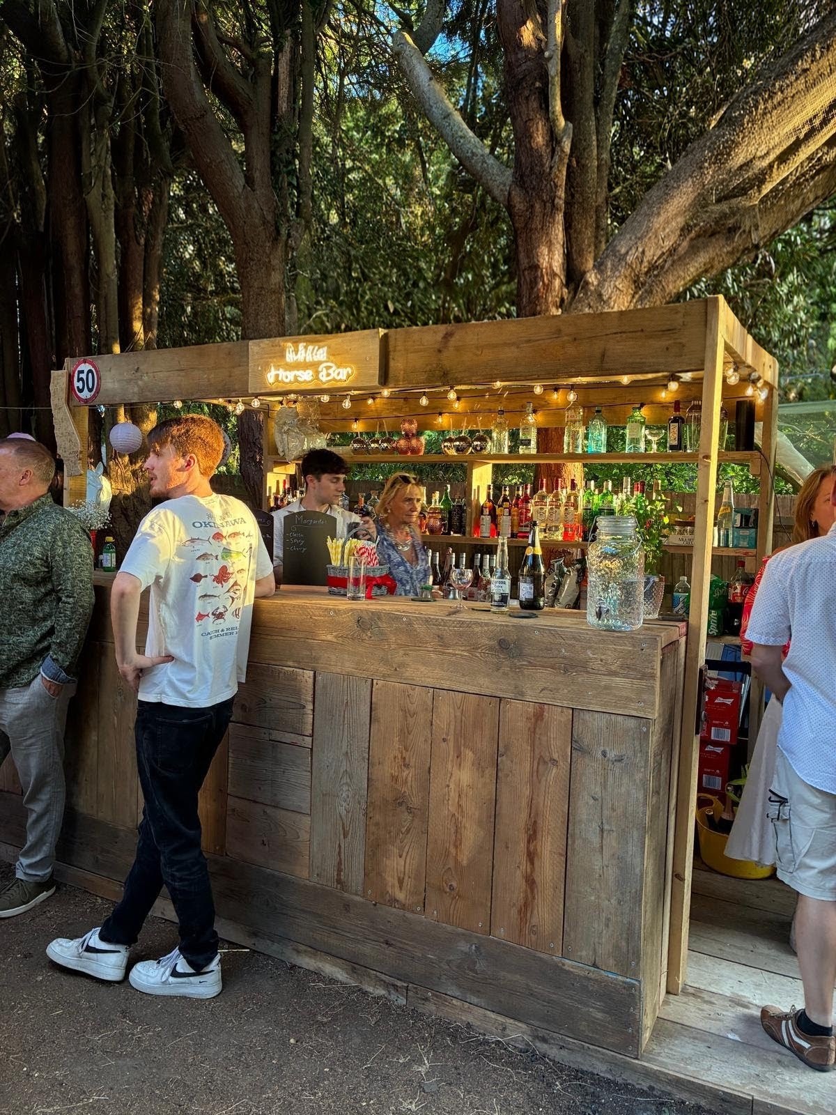 A handcrafted wooden garden bar in use at an outdoor party with guests